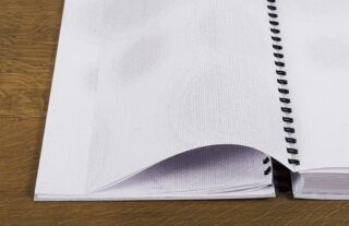 Eine Nahaufnahme eines offenen Spiralnotizbuchs mit leeren, leicht strukturierten Seiten, das auf einer Holzoberfläche liegt.