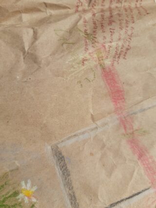 Ein zerknülltes Stück braunes Papier mit blassrotem handgeschriebenem Text, einer roten Linie und Buntstiftzeichnungen einer weißen Blume und grüner Blätter.