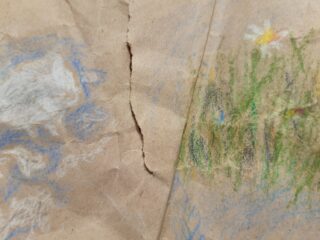 Eine Nahaufnahme von braunem Papier mit einem Riss in der Mitte, mit Buntstiftzeichnungen einer weißen Wolke auf der linken Seite und einer weißen Blume mit grünem Gras auf der rechten Seite.