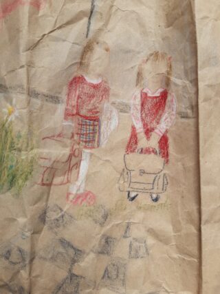 Eine zerknitterte Zeichnung zeigt zwei Kinder in roten Outfits mit Schultaschen in den Händen, die nebeneinander auf einem gemusterten Untergrund stehen. Ihre Gesichter sind ausdruckslos.