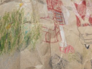 Ein zerknülltes Stück Papier mit einer Kinderzeichnung, die in Rot einen Teil einer Person und links eine Grasfläche mit Blumen zeigt.