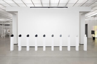 Neun Skulpturen in den Farben Schwarz und Weiß werden auf einzelnen weißen Sockeln in einer modernen, minimalistischen Galerie mit weißen Wänden und Decken ausgestellt.