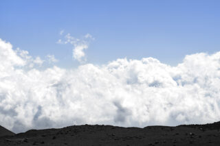 Felsiges Gelände im Vordergrund mit einer riesigen Wolkenfläche und klarem blauen Himmel im Hintergrund.