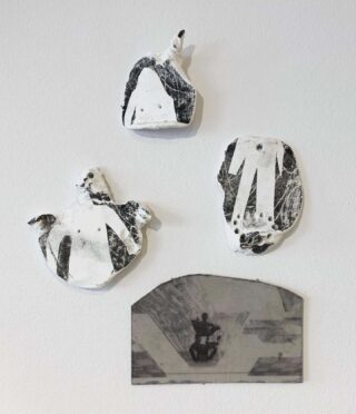 Drei abstrakte schwarz-weiße Gipsskulpturen und ein rechteckiger Spiegel sind an einer schlichten weißen Wand angebracht.