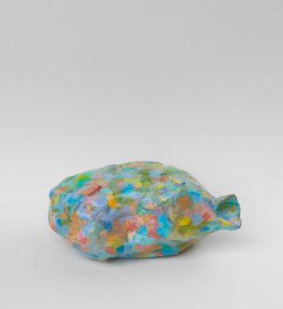 Auf einem schlichten weißen Hintergrund befindet sich ein kleines, unregelmäßig geformtes Keramikobjekt mit schmaler Tülle, das mit bunten Farbklecksen bedeckt ist.