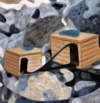 Zwei kleine Holzkisten mit Öffnungen sind durch eine schwarze Rampe verbunden und zwischen unterschiedlich großen Steinen platziert.