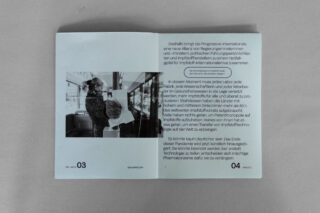 Ein aufgeschlagenes Heft zeigt auf der linken Seite ein Schwarz-Weiß-Foto einer Person mit Maske in öffentlichen Verkehrsmitteln und auf der rechten Seite einen deutschen Text zur COVID-19-Impfung.