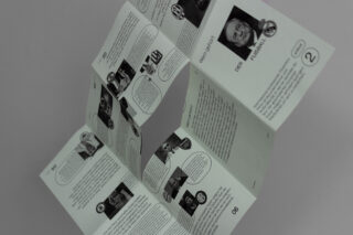 Eine gefaltete Broschüre ist geöffnet. Sie zeigt Seiten mit Text, nummerierten Abschnitten und kleinen Schwarzweißfotos von Personen. Die Broschüre scheint auf Deutsch zu sein.