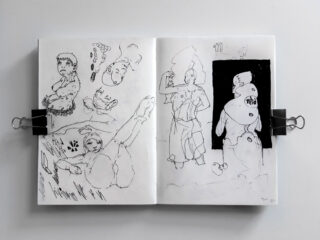 Ein offenes Skizzenbuch zeigt abstrakte Tuschezeichnungen menschlicher Figuren und Gesichter, wobei auf der rechten Seite eine Figur vor einem schwarzen Hintergrund umrissen ist.