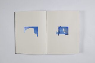 Ein offenes Buch zeigt zwei Seiten mit jeweils einem ausgeschnittenen rechteckigen Abschnitt, unter dem sich ein Bild des blauen Himmels befindet.