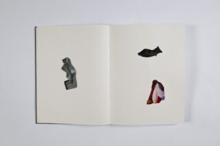 Ein offenes Buch mit zwei Seiten, die jeweils eine einzelne ausgeschnittene Form enthalten; der linke Ausschnitt zeigt ein graues Objekt und der rechte Ausschnitt zeigt einen Teil eines bunten Stoffes darunter.