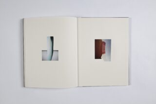 Ein offenes Buch zeigt zwei Seiten, jede mit einem kleinen Foto in der Mitte eines größtenteils leeren weißen Raums. Das linke Foto ist abstrakt, das rechte zeigt eine rote Struktur vor dem Himmel.