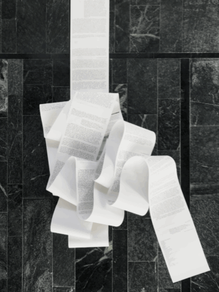 Auf einem dunklen Marmorfliesenboden liegt ein langes, gewelltes Blatt Papier mit dichtem Text.