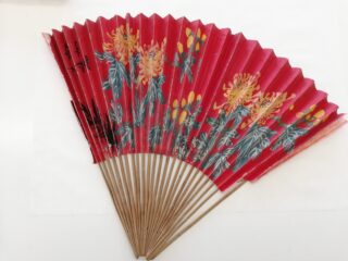 Ein roter Handfächer aus Papier mit einem Blumenmuster in Gelb und Grün und Holzrippen auf weißem Hintergrund.