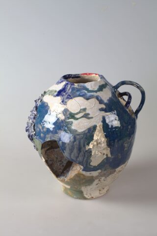 Eine unregelmäßig geformte Keramikvase mit einem Loch in der Nähe des Bodens, einem einzelnen Griff und einer blau, grün und weiß strukturierten Oberfläche.