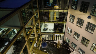 Blick auf den Innenhof eines modernen Gebäudes bei Nacht, mit Lichterketten, Glasfenstern und Schnee auf dem Boden und den Dächern.