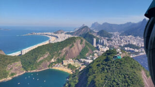 Luftaufnahme von Rio de Janeiro mit Stränden, Bergen, Stadtgebäuden und grünen Hügeln unter einem klaren blauen Himmel.