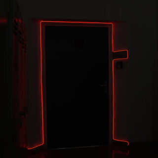 Eine dunkle Tür, umrandet von einem roten Neonlichtstreifen, der einen leuchtenden Rahmen um die Tür bildet und sich bis zu einer horizontalen Linie auf der rechten Seite erstreckt.