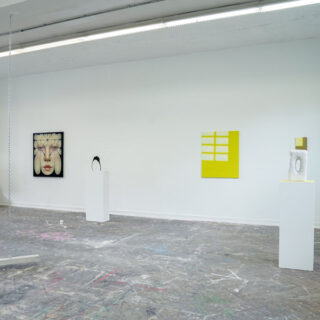 Eine minimalistische Kunstgalerie mit abstrakten Skulpturen auf weißen Sockeln und modernen Gemälden, darunter ein Gesicht, die an weißen Wänden ausgestellt sind; der Boden ist mit Farbe bespritzt.