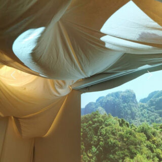 Eine Stoffdecke, durch deren Löcher das Licht fällt, neben einer Wandprojektion einer grünen Berglandschaft.