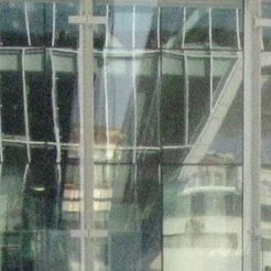 Glasfenster, die das verzerrte Bild eines nahegelegenen Gebäudes mit sichtbaren Fensterrahmen und architektonischen Details widerspiegeln.