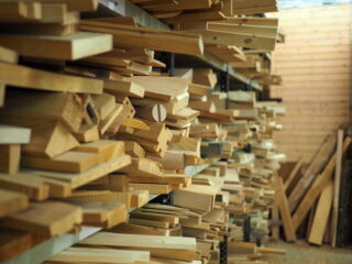 Stapel unterschiedlich geschnittener Holzbretter werden in einer Werkstatt oder einem Holzlager auf Metallregalen angeordnet.