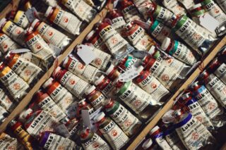 Dicht an dicht stehen Farbtuben der Marke LUKAS in verschiedenen Farbtönen, teilweise mit handbeschrifteten Etiketten an den Verschlüssen.