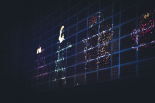 Auf einer dunklen Wand mit Gittermuster sind neonfarbene Umrisse von Retro-Videospielfiguren zu sehen.