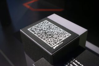 Ein schwarzer Ausstellungsständer weist in der unteren rechten Ecke ein weißes, kompliziertes geometrisches Muster mit der Aufschrift „gotth //“ auf.