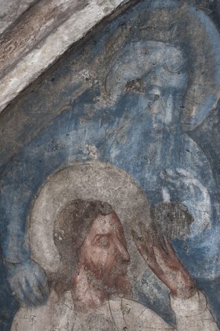 Ein verwittertes Fresko, das einen bärtigen Mann mit einem Heiligenschein zeigt, der seine Hand erhebt, mit einer schwach blauen Figur und einem zweiten Heiligenschein über ihm.