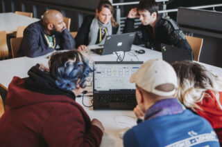 Fünf Personen sitzen mit Laptops um einen Tisch, arbeiten zusammen und betrachten digitale Diagramme auf einem Laptop-Bildschirm.