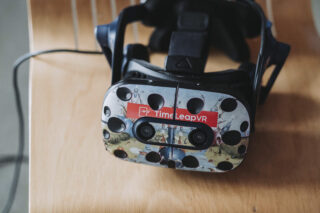 Ein Virtual-Reality-Headset mit der Aufschrift „Time Leap VR“ liegt mit angeschlossenem Kabel nach vorne gerichtet auf einer Holzoberfläche.
