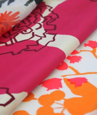 Nahaufnahme eines bunten Stoffes mit kräftigen Blumenmustern in Rosa-, Orange- und Cremetönen, die sich auf einer flachen Oberfläche überlappen.