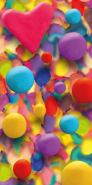 Bunte Kugeln und eine große rosa Herzform liegen auf einem lebendigen, mehrfarbigen abstrakten Hintergrund.