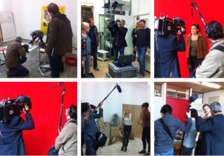 Ein Filmteam zeichnet mit Kameras und Galgenmikrofonen vor rotem und neutralem Hintergrund Interviews und Aktivitäten mit mehreren Personen in einem Kunstatelier auf.