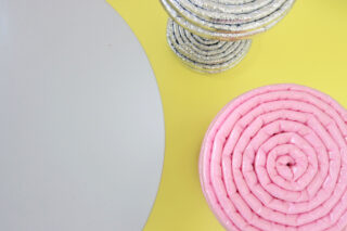 Ein rundes rosafarbenes Objekt und ein kleineres silbernes Objekt, beide aufgerollt, liegen auf einer gelben Fläche neben einer großen grauen Kreisform.