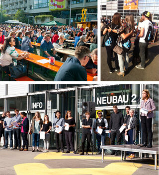 Eine große Veranstaltung im Freien mit Menschen, die an Tischen sitzen, Gruppen, die sich unterhalten, und einer Reihe von Einzelpersonen in der Nähe eines Gebäudes mit der Aufschrift „NEUBAU 2“ und „INFO“.