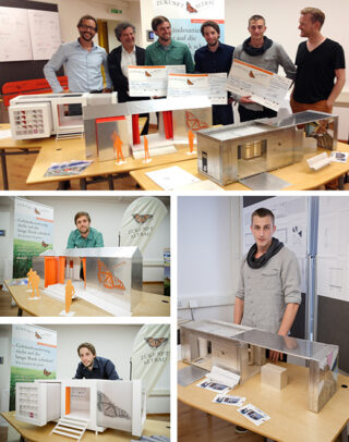 Eine Gruppe von Menschen und Einzelpersonen posiert mit großen Schecks und Architekturmodellen, die in einem Klassenzimmer auf Tischen ausgestellt sind.