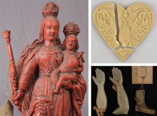 Eine rote Statue einer gekrönten Frau, die ein Kind hält, ein Relief in Form eines gebrochenen Herzens und drei kleine geformte Hand- und Armstücke.