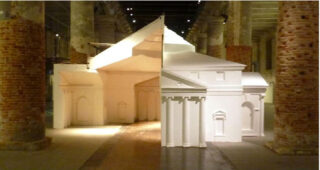 Im Innenbereich wird zwischen Ziegelsäulen eine weiße architektonische Skulptur ausgestellt, deren klassische Fassade und geometrische Formen durch dramatische Beleuchtung hervorgehoben werden.