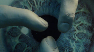 Drei graue Finger sind vor einer detaillierten Nahaufnahme einer blaugrünen menschlichen Iris und Pupille positioniert.