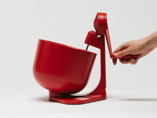 Eine Hand bedient eine rote Küchenmaschine mit einer großen Rührschüssel und minimalistischem Design vor einem schlichten weißen Hintergrund.