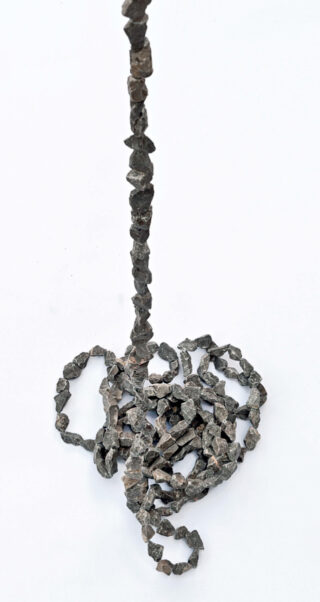 Eine vertikale Reihe unregelmäßig geformter dunkler Steine oder Mineralien, wobei der untere Teil locker auf einer weißen Oberfläche aufgerollt ist.