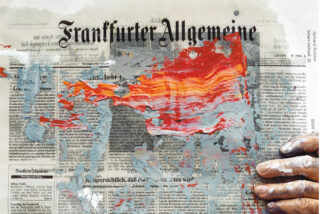 Eine deutsche Zeitung, die teilweise mit kräftigen roten, orangefarbenen und grauen Farbstrichen bedeckt ist. In der unteren rechten Ecke ist eine mit Farbe verschmierte Hand zu sehen.