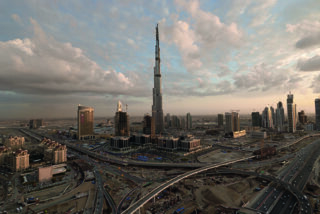 Luftaufnahme der Skyline von Dubai mit dem Wolkenkratzer Burj Khalifa, umgeben von modernen Gebäuden und Straßen unter einem bewölkten Himmel.