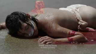 Eine Person mit kurzen Haaren liegt mit dem Gesicht nach unten auf einer nassen Oberfläche, teilweise bedeckt mit Sand und Blut, mit dem Untertitel „Ihrer Grausamkeit sind keine Grenzen gesetzt.“.