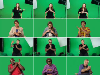 Zwölf Personen sitzen vor grünen Bildschirmen und führen Gesten in Gebärdensprache aus. Im Hintergrund sind Studiolichter zu sehen.