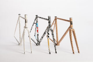 Drei Fahrradrahmen mit markanten geometrischen und gestreiften Mustern stehen aufrecht auf einem weißen Hintergrund.
