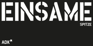 In großer weißer Schrift auf schwarzem Grund steht „EINSAME SPITZE“, in der unteren linken Ecke erscheint „ADK“.