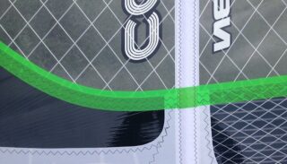 Nahaufnahme eines Segels mit weißen und schwarzen Nähten, grünem Besatz, transparenten Abschnitten und geometrischen Mustern.